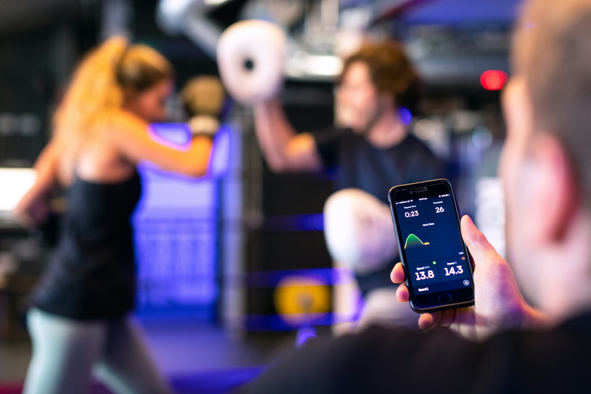 Coach tracking a client's session data on a phone on the gym floor