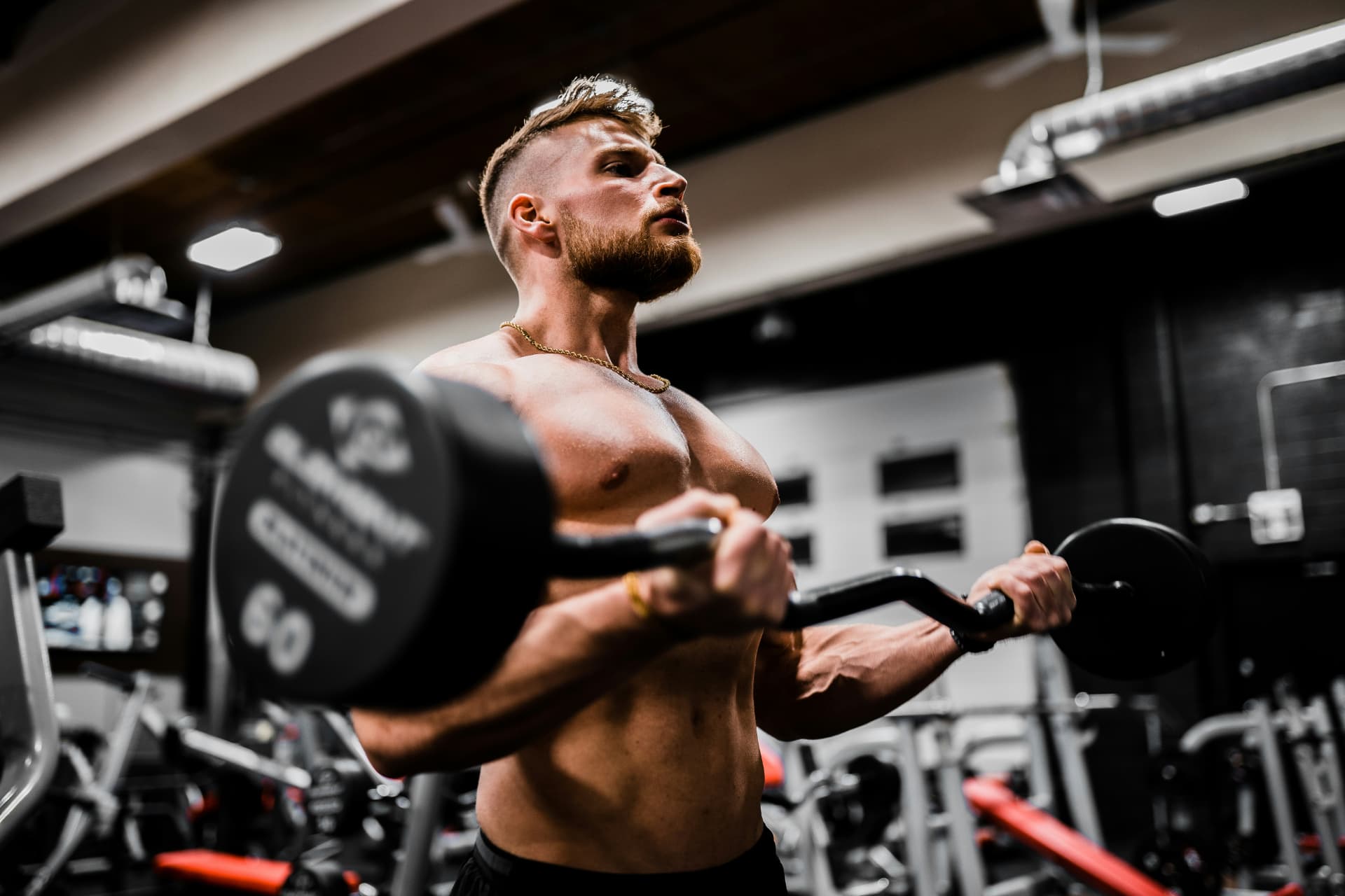 Trainer coaching a barbell curl in a busy gym